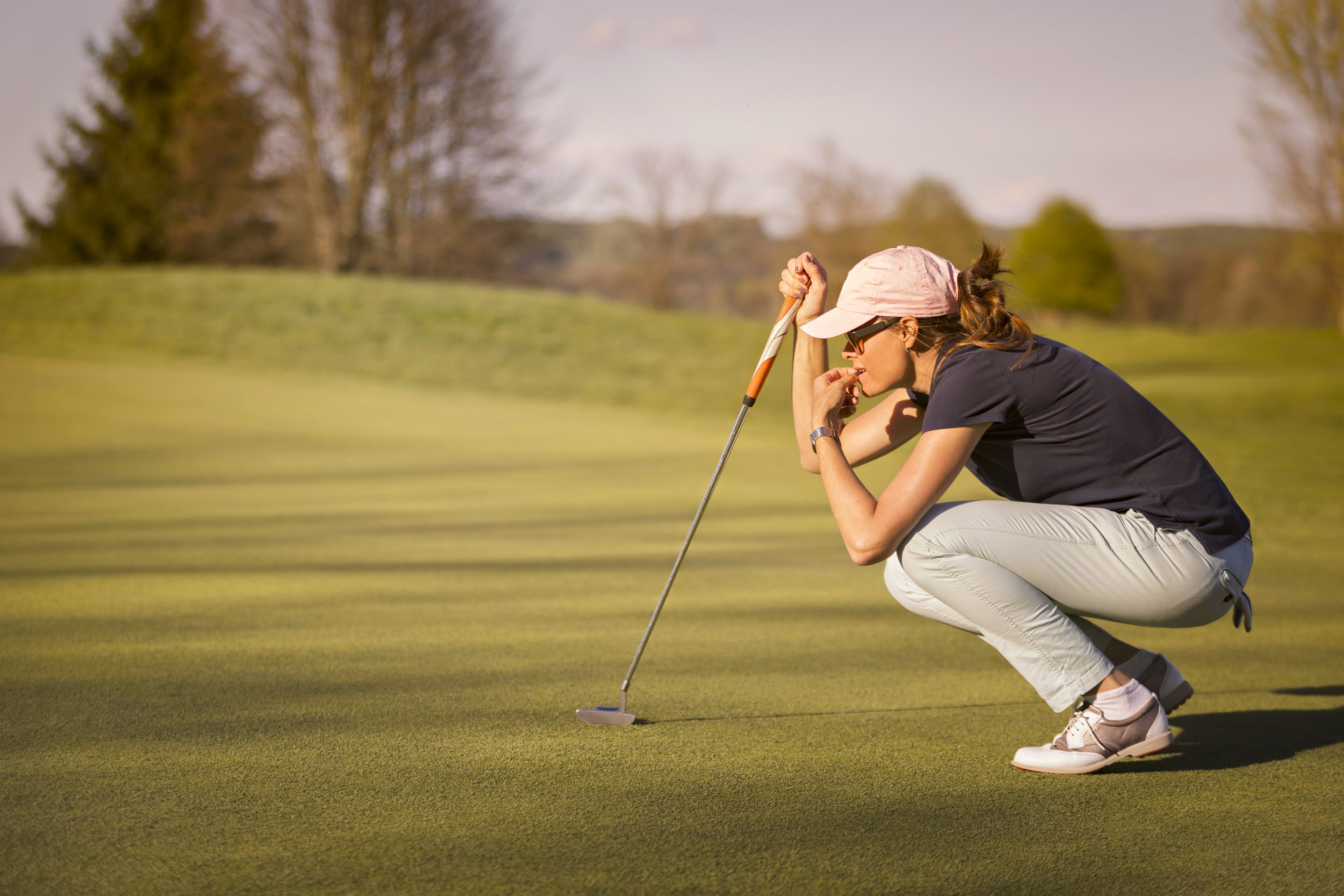 Woman,Golf,Player,Crouching,And,Study,The,Green,Before,Putting